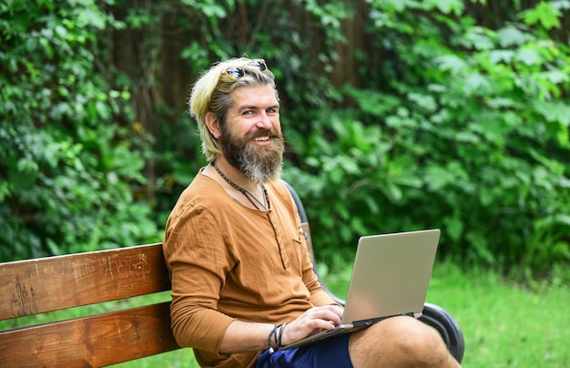Agile business Bearded guy sit on bench in park nature background Work and relax Fresh air Mobile internet You can work anywhere Online shopping Working online Hipster inspired work in park