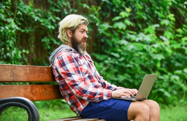 Agile business mature student working on computer go shopping\
on cyber monday bearded man on bench with laptop online distant\
education hipster inspired to work in park preparing to the\
exams