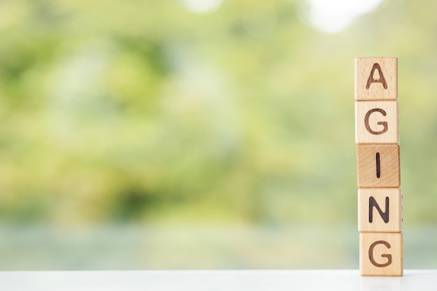 Aging word is written on wooden cubes on a green summer background Closeup of wooden elements