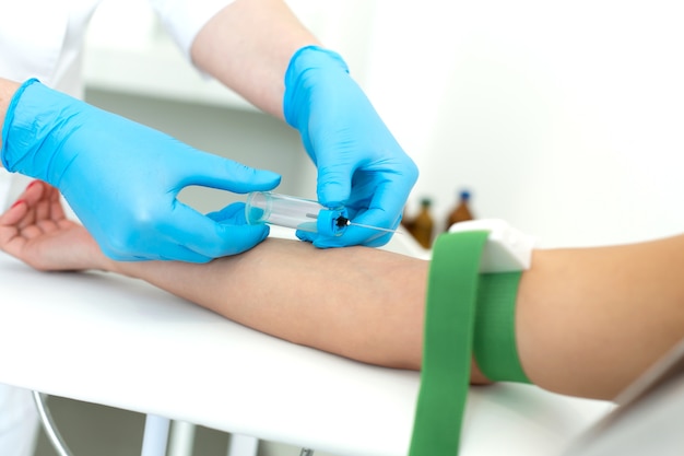 Agloved nurse inserts a needle into vein on the patients arm and draws blood into a vacuum container