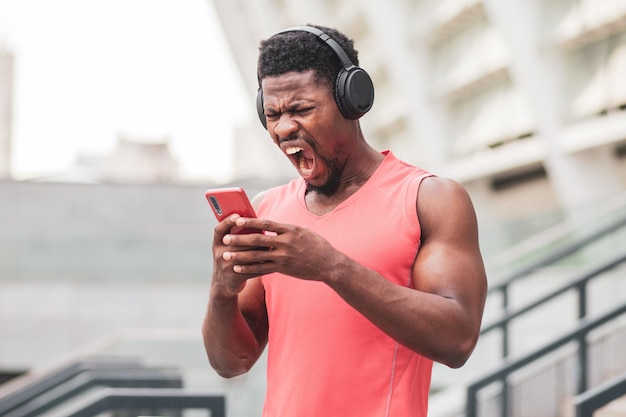 Agressieve afrikaanse man met koptelefoon die in de telefoon schreeuwt tegen de achtergrond van de stad