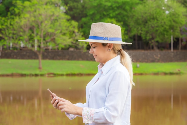 Donna agroalimentare che indossa cappello e jeans alla fine di una giornata lavorativa in possesso di un cellulare