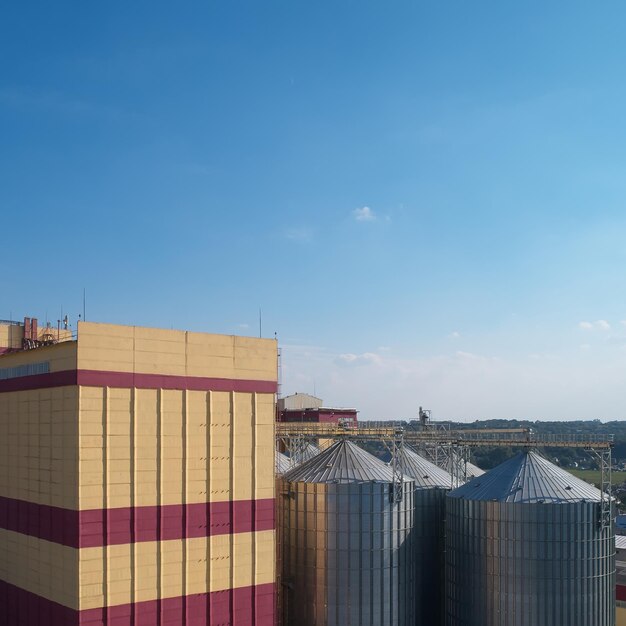 Сельскохозяйственное силосное хранилище и сушка зерна пшеницы, кукурузы, сои на фоне голубого неба с облаками