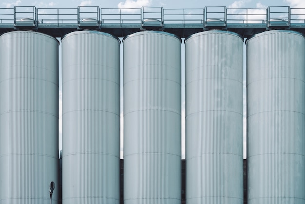 Foto silos agricoli. conservazione e essiccazione di cereali, grano, mais, soia, girasole. esterno di un edificio industriale. primo piano di grandi contenitori metallici d'argento. sfondo di carri armati agricoli con spazio di copia.