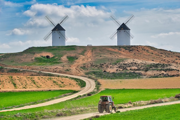 Agricultural tractor circulating in the field with a hill with large windmills in the background.