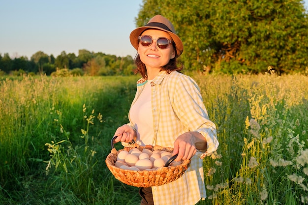 Agriculture, farming organic eco products. Woman farmer holding basket of fresh eggs, nature, garden, countryside background