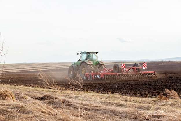 Agricoltura, trattore preparazione terreno con coltivatore a letto di semina come parte delle attività di pre-semina all'inizio della stagione primaverile dei lavori agricoli nei terreni agricoli.