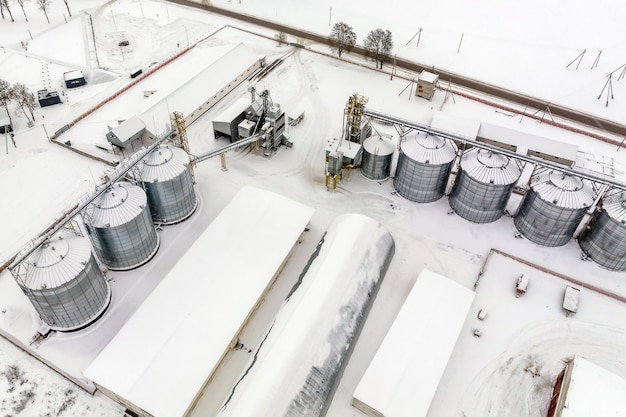 Agro silos granary elevator in winter day in snowy field Silos on agroprocessing manufacturing plant for processing drying cleaning and storage of agricultural products flour cereals and grain