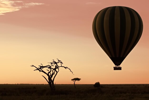 Foto una mongolfiera che vola sopra un paesaggio arido al tramonto nel serengeti, in tanzania