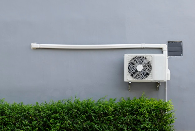 Air compressor on gray wall with green bush