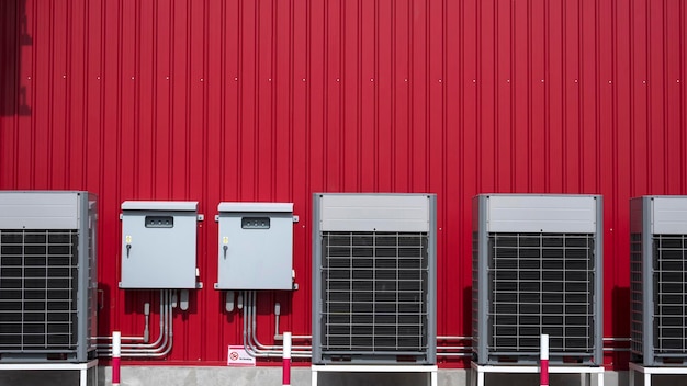 Air compressors with electric control cabinets and pipelines on red metal wall outside of building