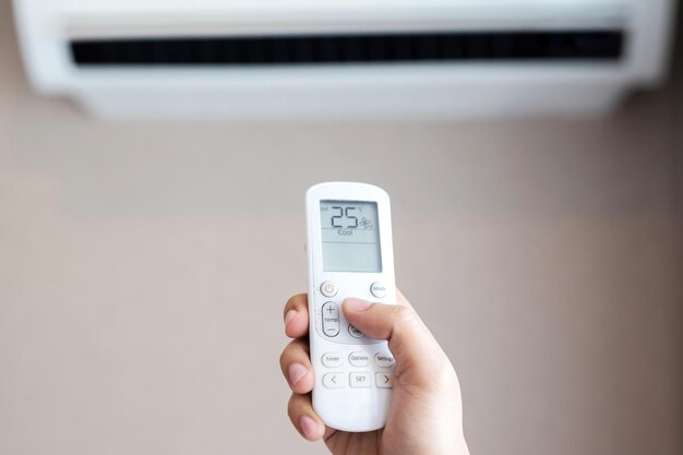 Air conditioner inside the room with close up man hand holding using directed operating remote controller