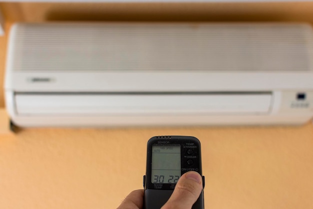 Air conditioner inside the room with man operating remote controller.