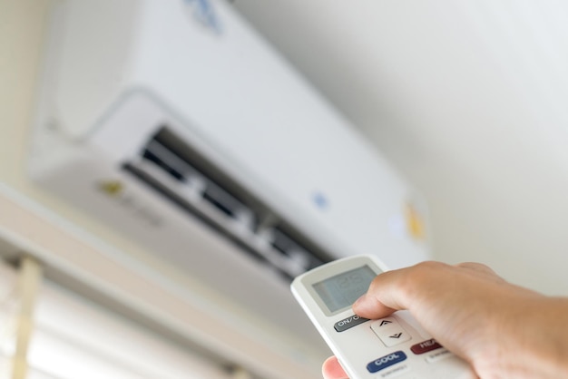 An air conditioner in a room with a young person using a remote\
control is turning on the air conditioner during the sweltering\
day