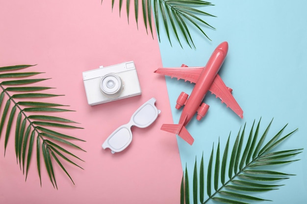 Air plane camera sunglasses and palm green leaves on pink blue pastel background Travel concept Tropical composition Top view Flat lay