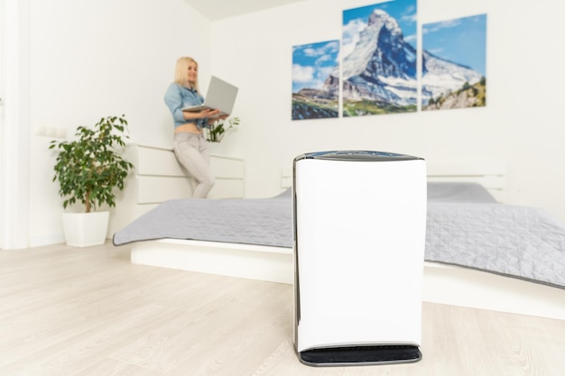 Air purifier in a room, woman working with laptop with filter for clean room.