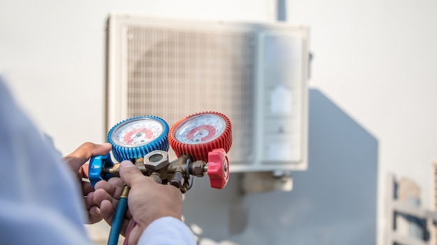 Air repairman using manifold gauge to filling industrial factory air conditioners