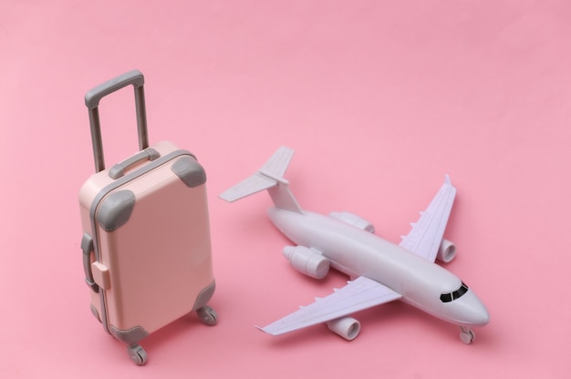 Air travel concept. Mini plastic travel suitcase, air plane on pink background.