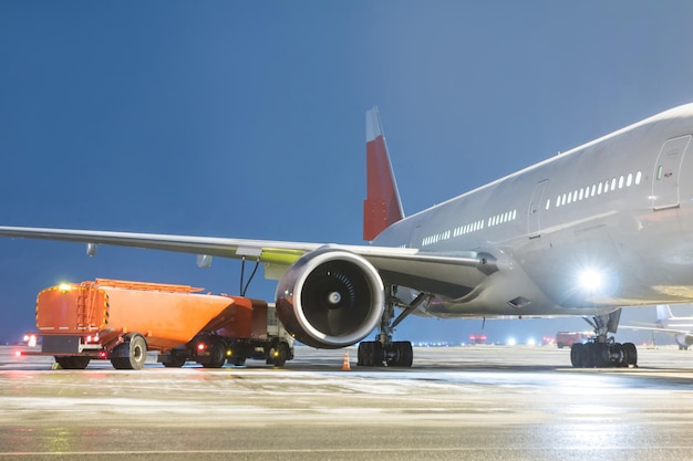 Airfield tanker refuels a widebody passenger aircraft on the night airport apron