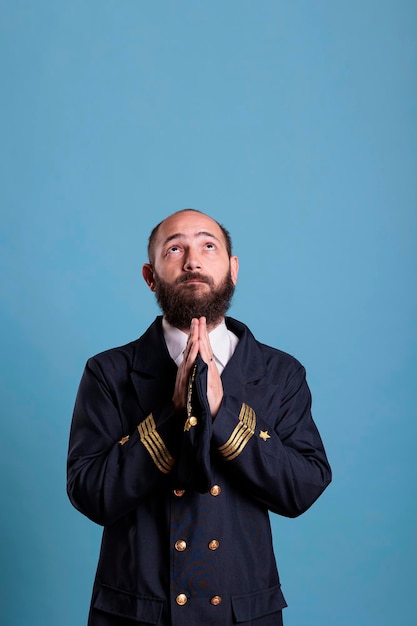 Airline pilot in uniform praying to gods, looking upwards,\
standing with folded hands gesture. religious plane captain\
pleasing, aviator worshiping before flight, praising