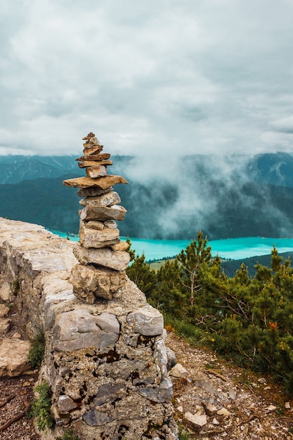 airn stack of stones mountain view of Alpine turquoise lake spruce forest low clouds in Bavaria