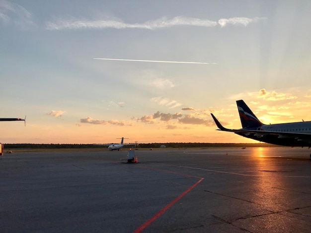 Airplane on airport runway against sky during sunset