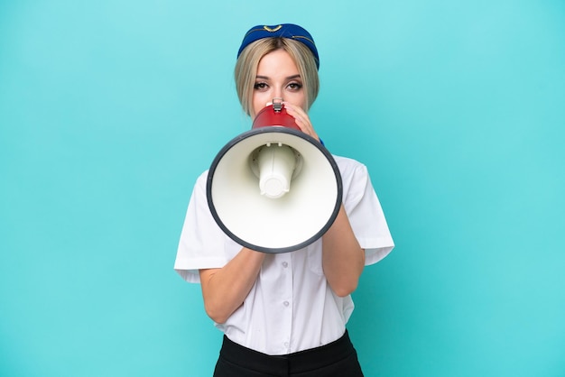 Airplane blonde stewardess woman isolated on blue background shouting through a megaphone