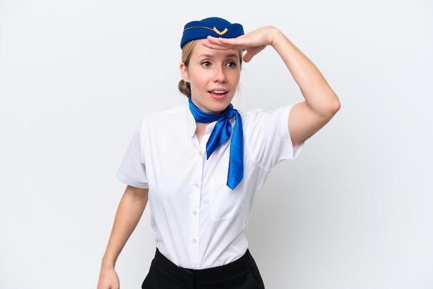 Foto donna bionda hostess dell'aeroplano isolata su sfondo bianco che guarda lontano con la mano per guardare qualcosa