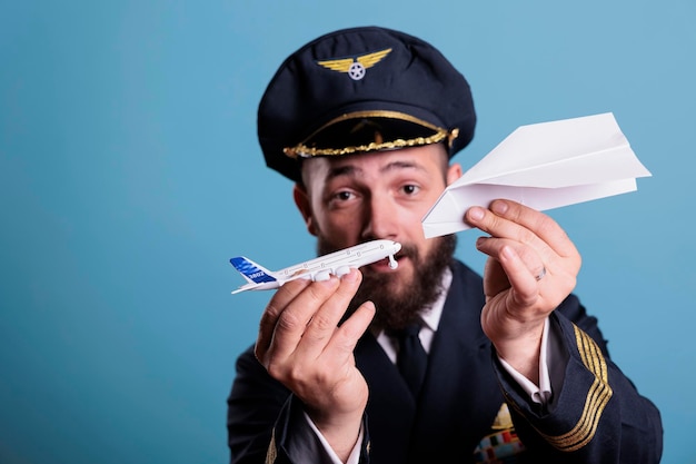 Airplane captain holding jet model and paper plane in hands\
front view, pilot demonstrating aircraft crash with aeroplane toys.\
professional aviation academy aviator on blue background