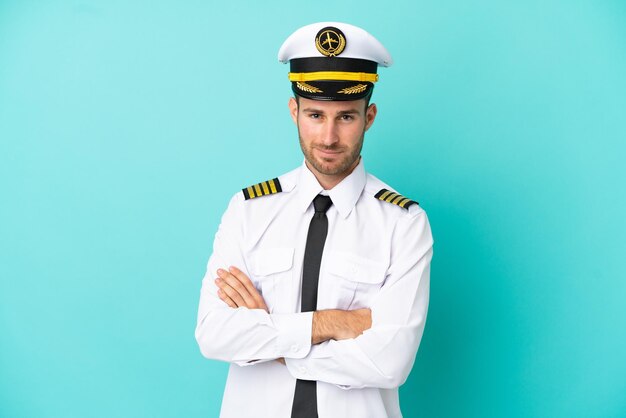 Airplane caucasian pilot isolated on blue background keeping the arms crossed in frontal position