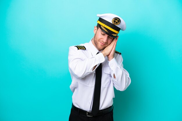 Airplane caucasian pilot isolated on blue background making sleep gesture in dorable expression