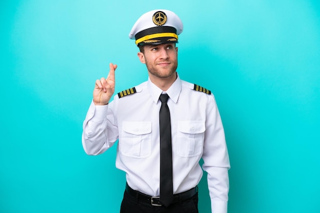 Airplane caucasian pilot isolated on blue background with fingers crossing and wishing the best