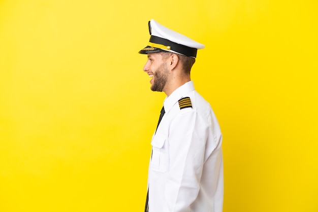 Airplane caucasian pilot isolated on yellow background laughing in lateral position