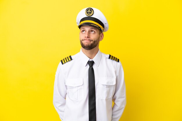 Airplane caucasian pilot isolated on yellow background and looking up