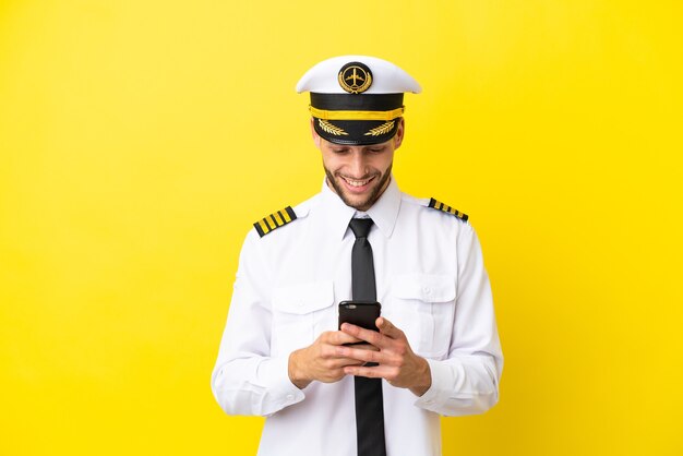 Пилот самолета кавказской изолирован на желтом фоне, отправляя сообщение с мобильного телефона
