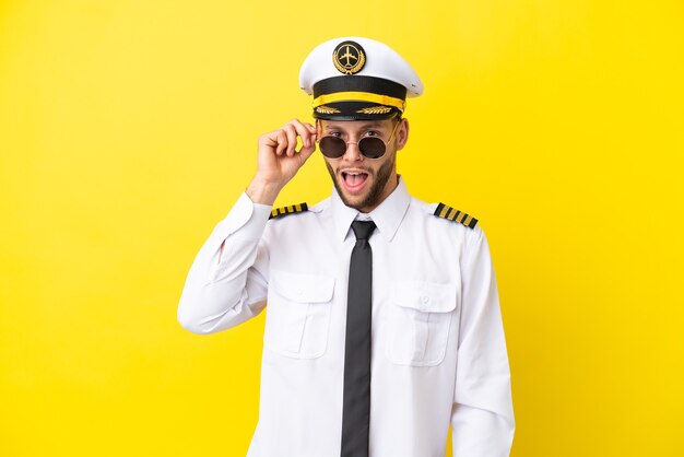 Airplane caucasian pilot isolated on yellow background with glasses and surprised