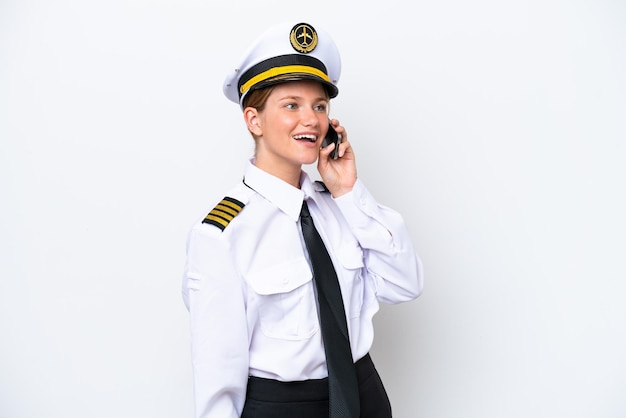 Airplane caucasian pilot woman isolated on white background keeping a conversation with the mobile phone