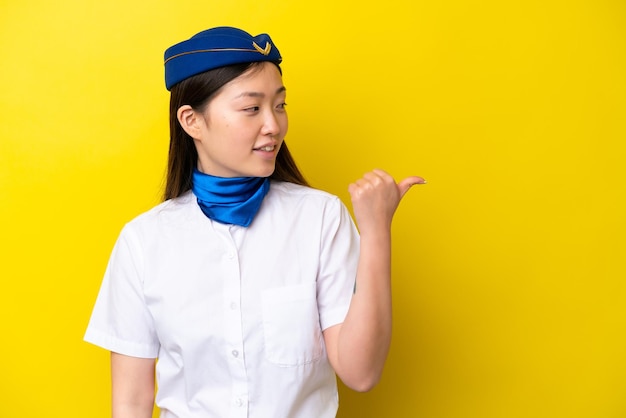 Airplane Chinese woman stewardess isolated on yellow background pointing to the side to present a product