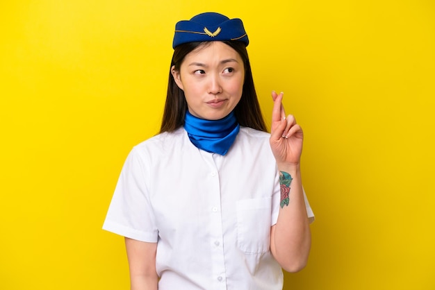 Airplane Chinese woman stewardess isolated on yellow background with fingers crossing and wishing the best