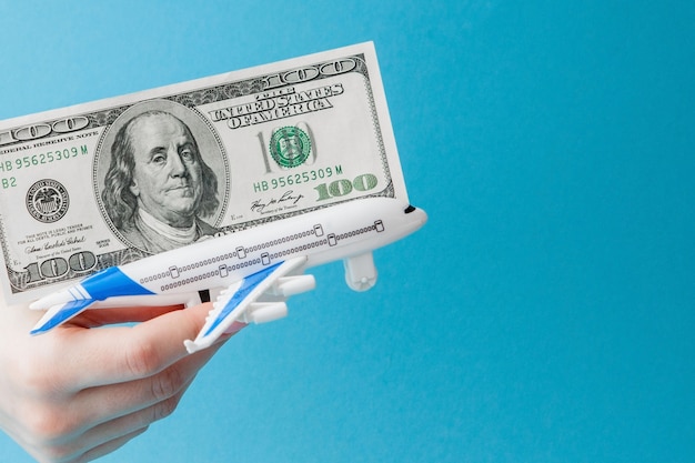Самолет и доллары в руке женщины на сини
