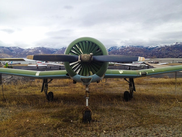 Photo airplane on field in front of mountains against cloudy sky