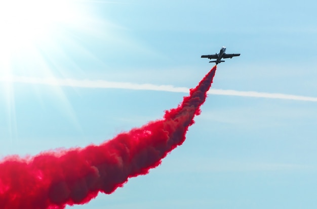 Mosca dell'aeroplano in zigzag con un fumo rosso della traccia nel cielo.