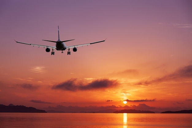 Airplane flying over tropical sea at beautiful sunset 