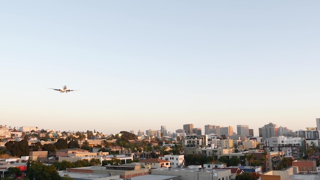 米国カリフォルニア州サンディエゴ空港への飛行機の着陸。日没、街のスカイライン、またはダウンタウンの都会の街並みに到着する飛行機の下。高層ビルと飛行機または航空機。空を飛んでいる旅客機。