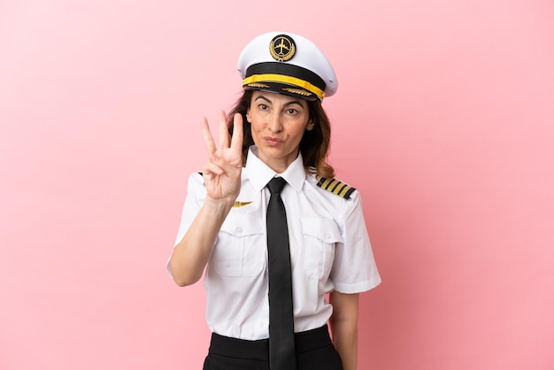 Airplane middle aged pilot woman isolated on pink background happy and counting three with fingers