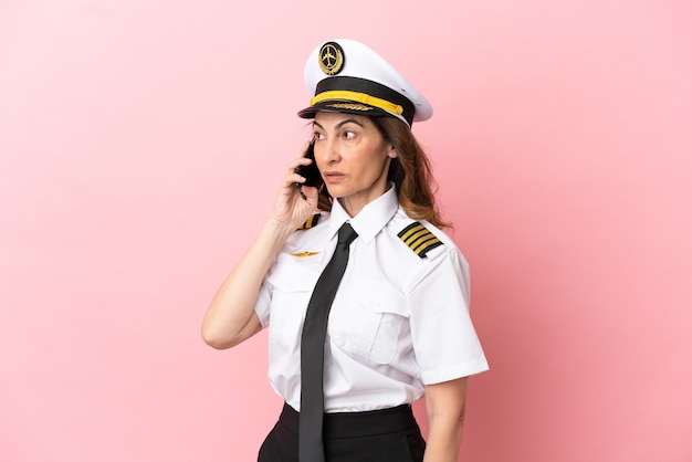 분홍색 배경에 격리된 비행기 중년 조종사 여성이 휴대전화와 대화를 유지하고 있다