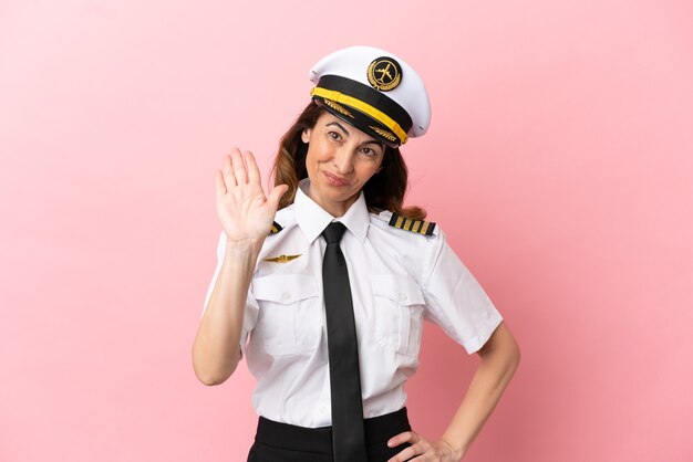 Airplane middle aged pilot woman isolated on pink background saluting with hand with happy expression