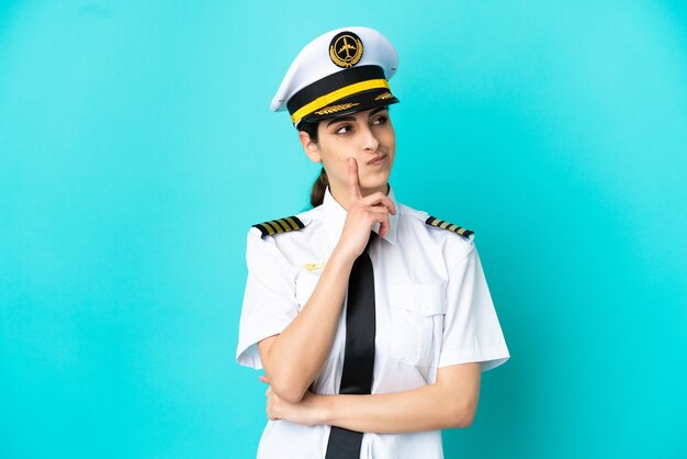 Airplane pilot caucasian woman isolated on blue background having doubts while looking up