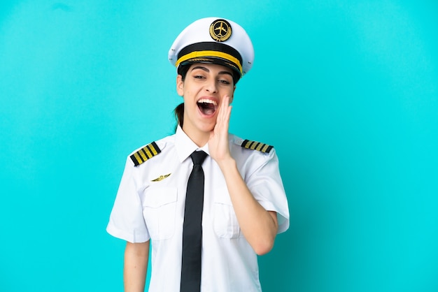 Airplane pilot caucasian woman isolated on blue background shouting with mouth wide open