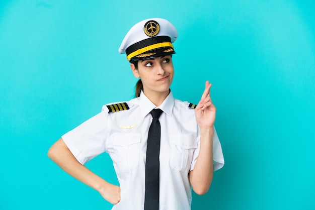 Кавказская женщина-пилот самолета изолирована на синем фоне со скрещенными пальцами и желает лучшего